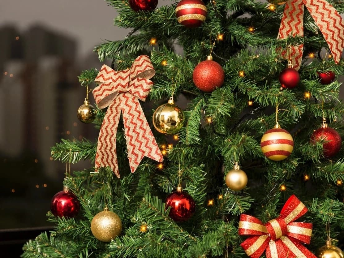 Árvore de Natal decorada com bolas vermelhas e douradas, laços listrados e luzes acesas
