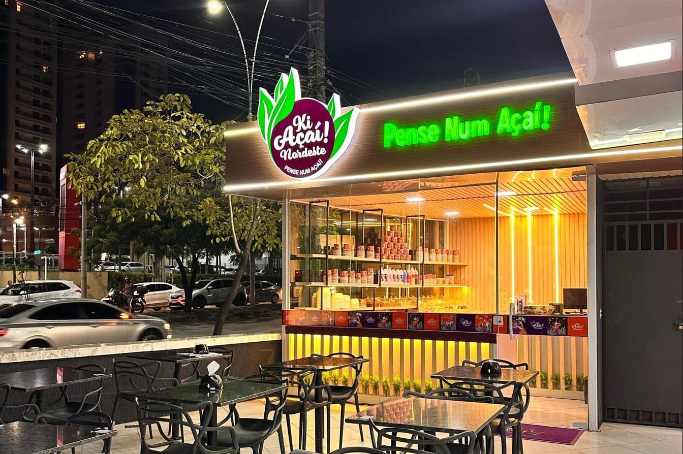 Loja Ki Açaí! Nordeste à noite, com letreiro Pense Num Açaí! em neon verde e mesas na calçada